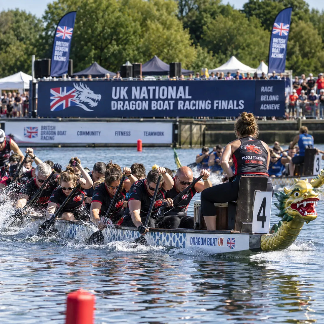 Dragon boat crew racing hard at the UK National Dragon Boat Racing Finals, paddles driving through the water as the drummer stands at the stern