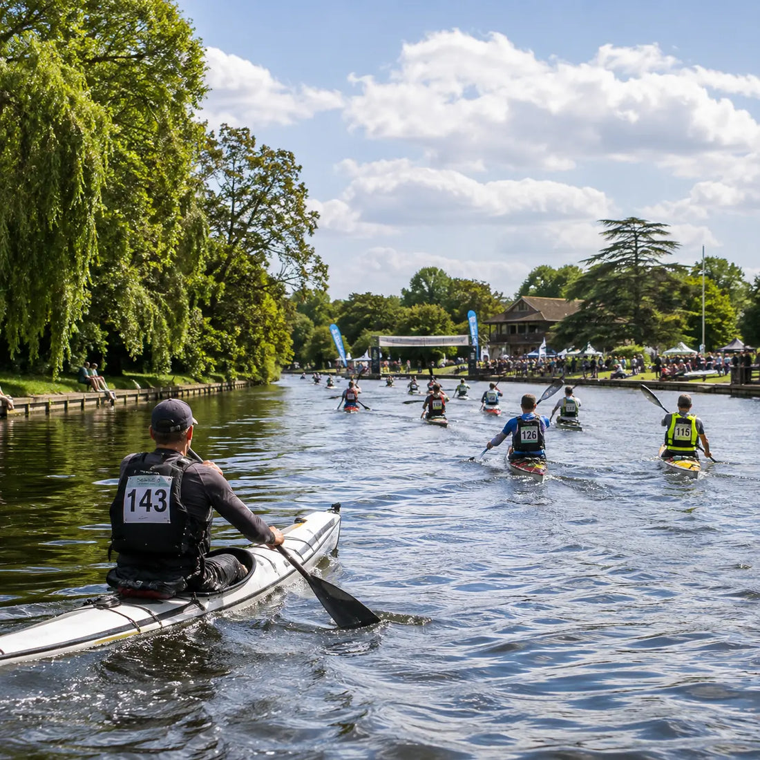 Kayak racers competing on the River Thames during an ultra paddle race, with a pack of competitors following behind the lead boat.