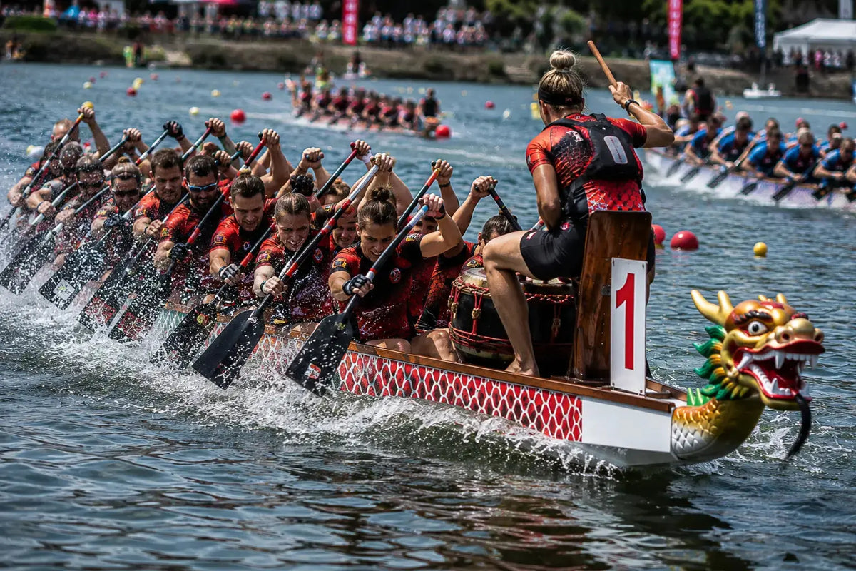 Dragon boat crew driving hard through a race, drummer calling the beat from the bow — dragon boat racing tees by Vector Paddle